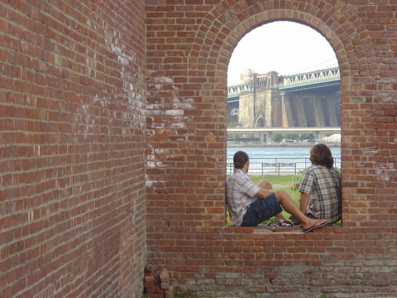 Dwóch chłopaków patrzących przez ceglane okno na most i rzekę Fot. Freeimages