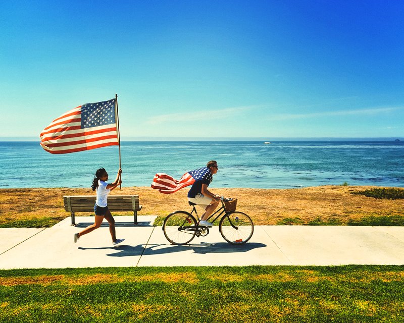 Kobieta z flagą USA goni rowerzystę z flagą USA Photo by frank mckenna on Unsplash