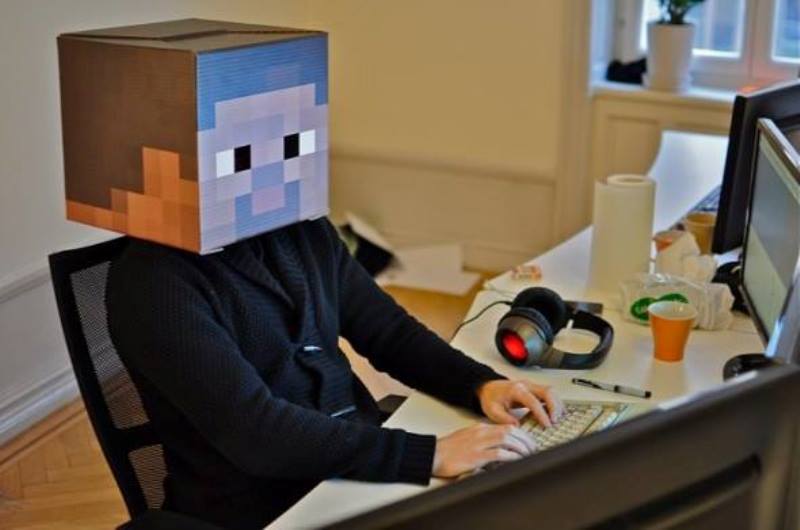Człowiek siedzący przy komputerze z kartonem na głowie z namalowaną twarzą z Minecrafta Fot. minecraft.pl