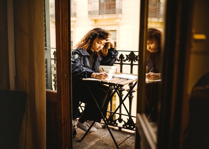 Dziewczyna pisząca na balkonie Photo by Kinga Cichewicz on Unsplash