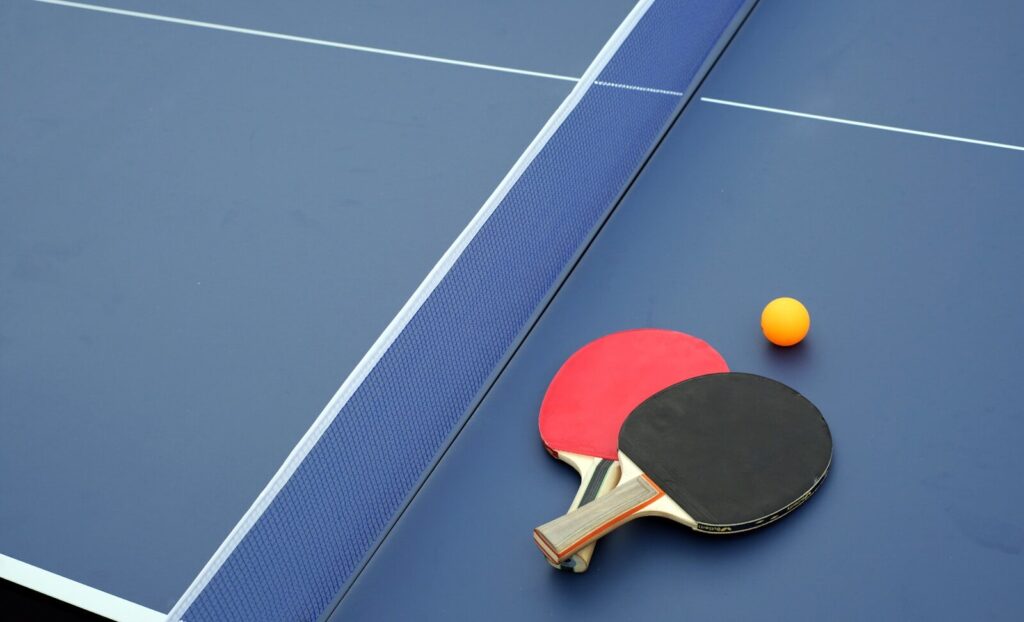 two ping pong paddles and a ping pong ball on a blue table