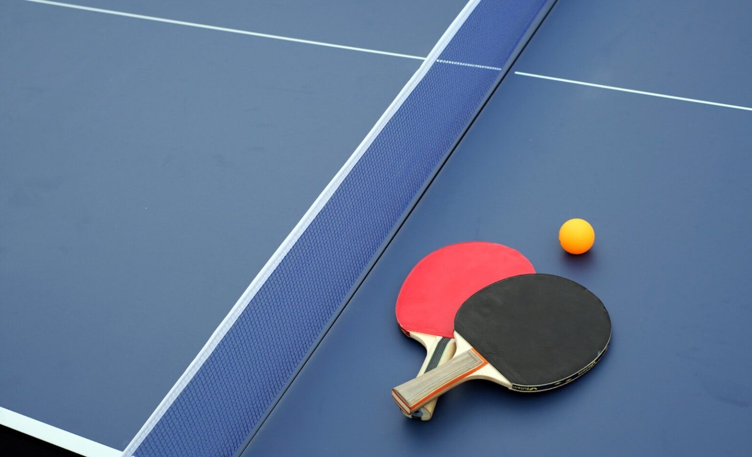 two ping pong paddles and a ping pong ball on a blue table