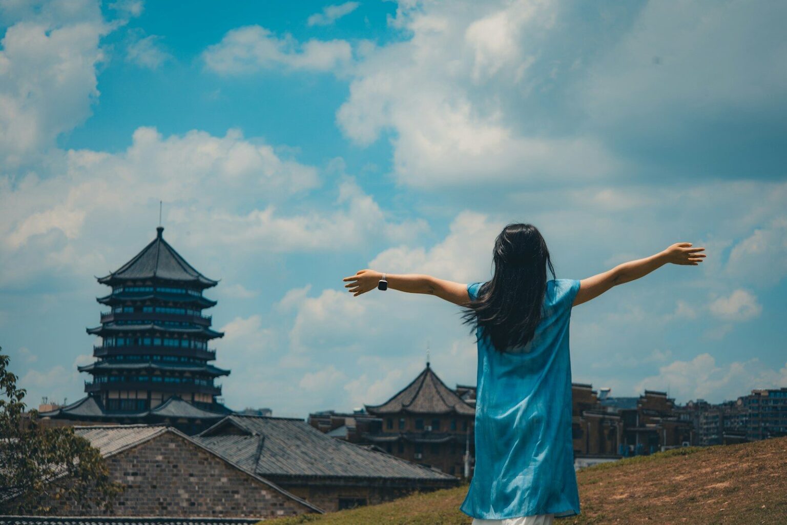Woman in blue dress with arms outstretched facing pagoda