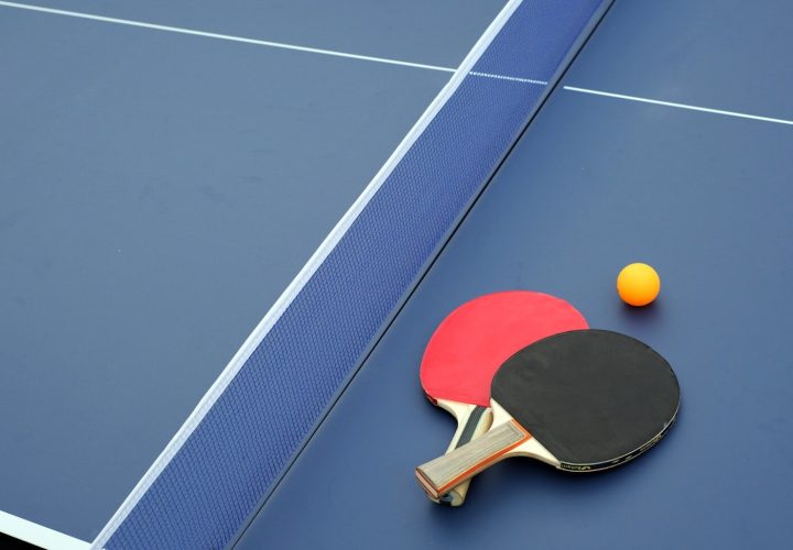 two ping pong paddles and a ping pong ball on a blue table