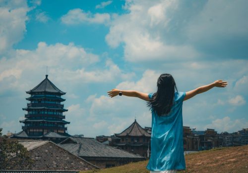 Woman in blue dress with arms outstretched facing pagoda
